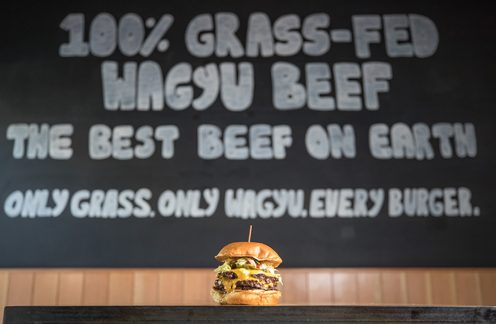 HiHo Triple Cheeseburger sitting on tabletop with HiHo wall art in background